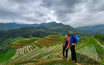 Trekking couple on Mu Cang Chai rice terraces, Vietnam, with lush green hills in the background.