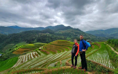 Trekking couple on Mu Cang Chai rice terraces, Vietnam, with lush green hills in the background.