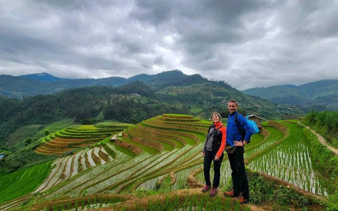 Trekking couple on Mu Cang Chai rice terraces, Vietnam, with lush green hills in the background.