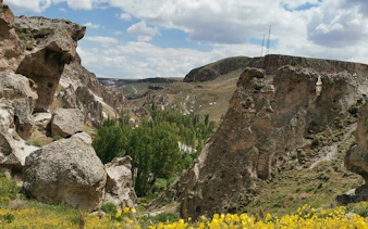Cappadocia rocky landscape with green valley and distant hills under a cloudy sky.
