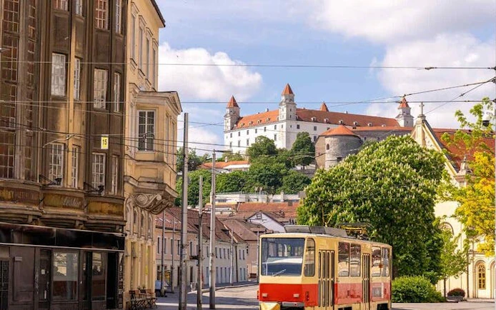 Tram passing by Bratislava Castle on a sunny day during a self-guided walking tour.