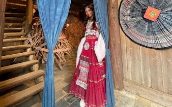 Person in traditional attire at Cat Cat Village, Sa Pa, near wooden staircase and woven decor.
