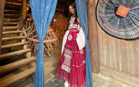 Person in traditional attire at Cat Cat Village, Sa Pa, near wooden staircase and woven decor.