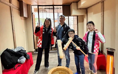 Family enjoying traditional mochi pounding experience in Japan, wearing cultural costumes.