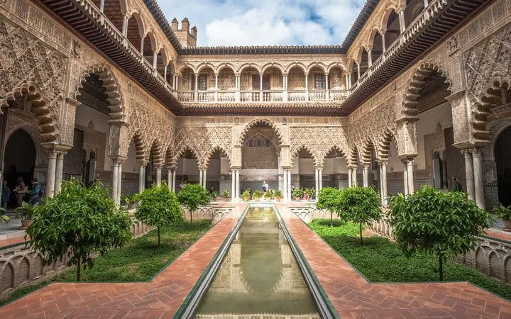 Alcázar of Seville courtyard with arches and reflecting pool on self-guided walking tour.