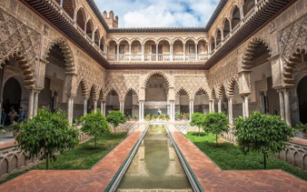 Alcázar of Seville courtyard with arches and reflecting pool on self-guided walking tour.