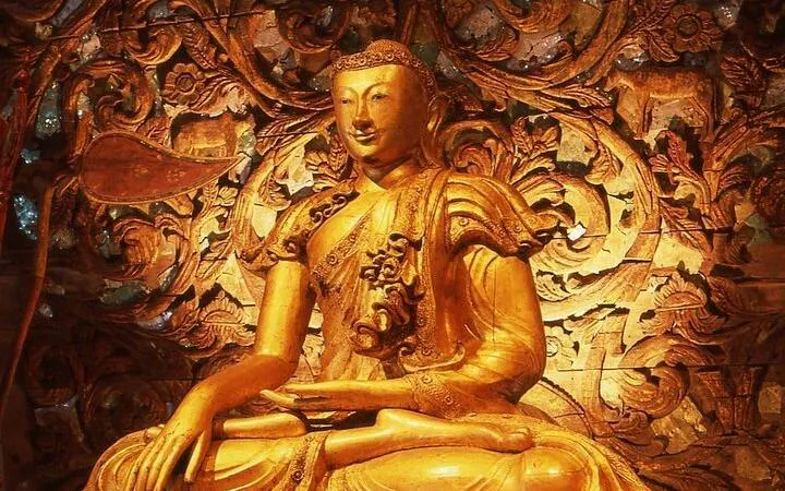 Golden Buddha statue at Wat Phra Kaew, Chiang Rai, with intricate floral carvings in the background.