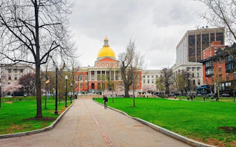 Massachusetts State House with golden dome in Boston, surrounded by park and city buildings.