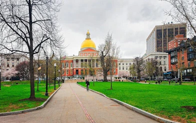 Massachusetts State House with golden dome in Boston, surrounded by park and city buildings.