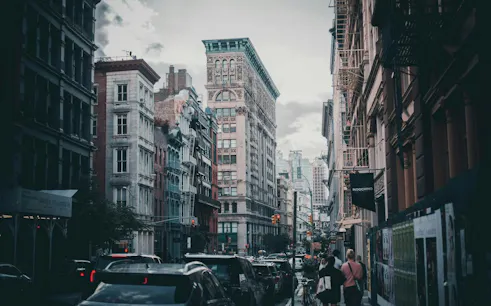 Street view of cast-iron buildings in SoHo, New York, with pedestrians and traffic.