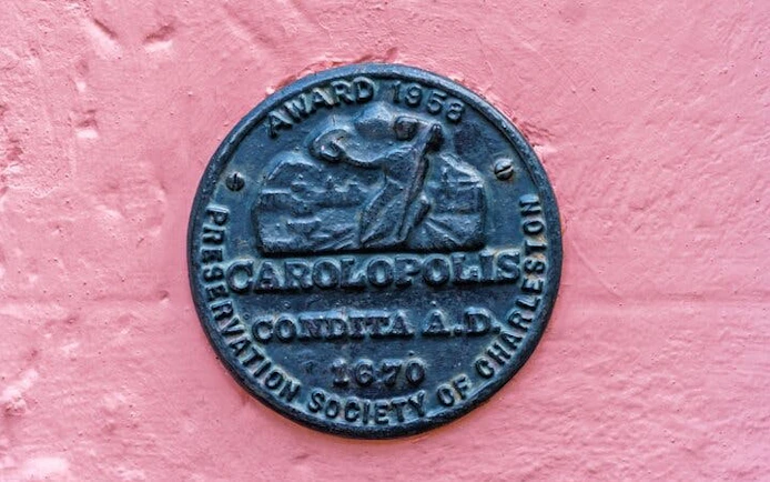 Carolopolis award plaque on pink wall in Charleston, highlighting historic preservation.