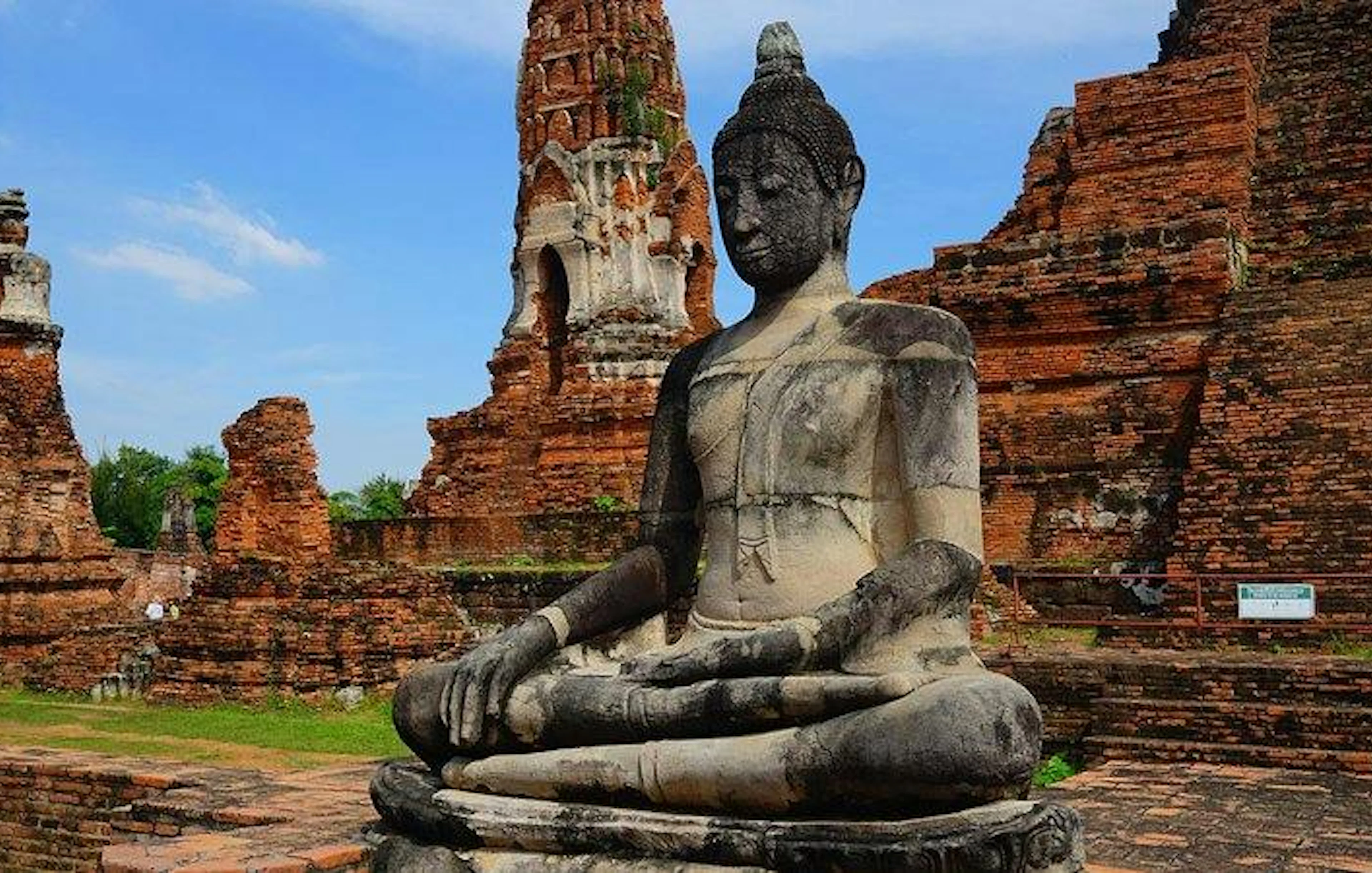 Buddha statue at Wat Mahathat, Ayutthaya, with ancient temple ruins in the background.