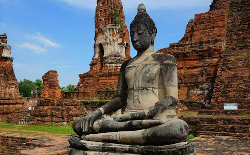 Buddha statue at Wat Mahathat, Ayutthaya, with ancient temple ruins in the background.
