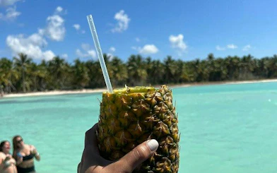 Pineapple drink held by a beachgoer at Saona Island, turquoise water and palm trees in the background.