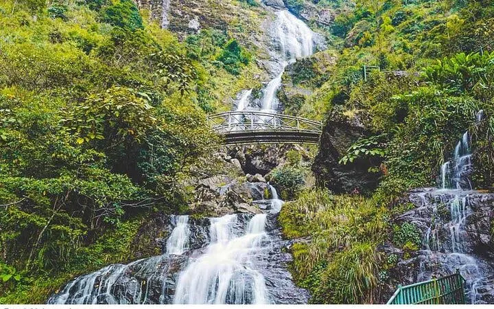 Waterfall cascading under a bridge surrounded by lush greenery in Sa Pa, Vietnam.