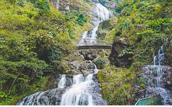Waterfall cascading under a bridge surrounded by lush greenery in Sa Pa, Vietnam.