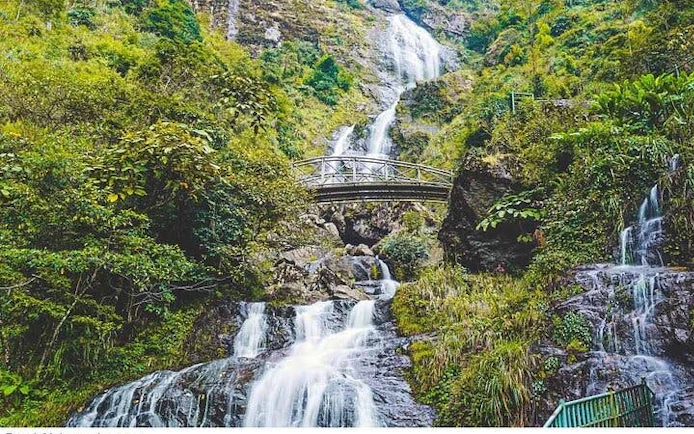 Waterfall cascading under a bridge surrounded by lush greenery in Sa Pa, Vietnam.