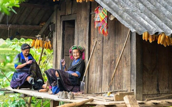 Ethnic villagers sitting on a wooden porch in Sa Pa, Vietnam, with corn hanging above.