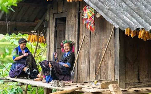Ethnic villagers sitting on a wooden porch in Sa Pa, Vietnam, with corn hanging above.