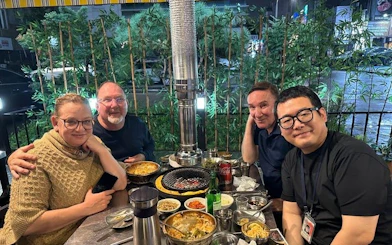 Small group enjoying Korean BBQ dinner in Gangnam, Seoul, with modern city backdrop.