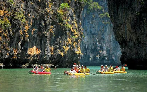 Sea kayaking group exploring Phang Nga Bay near limestone cliffs, Phuket.