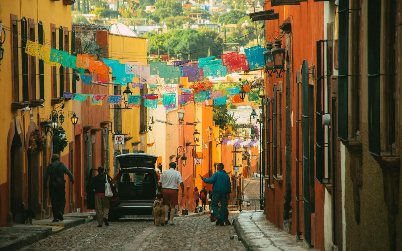Colorful street in San Miguel de Allende with papel picado banners and people walking.