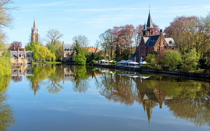 Bruges canal view with historic buildings and trees, part of self-guided city exploration game.