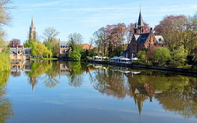 Bruges canal view with historic buildings and trees, part of self-guided city exploration game.