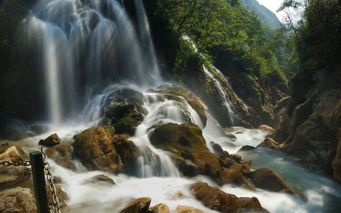 Silver Waterfall cascading over rocks surrounded by lush greenery in Sapa, Vietnam.