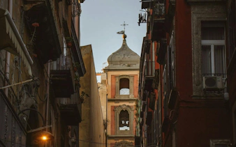 Narrow street view in Naples Historic Center with a church tower in the background.