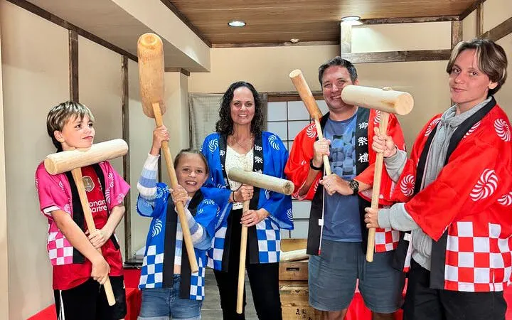 Group in traditional attire holding wooden mallets for mochi pounding experience in Japan.