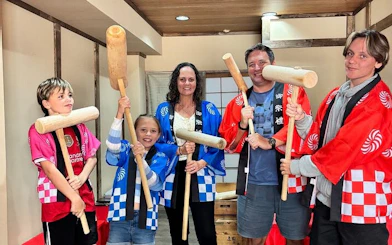 Group in traditional attire holding wooden mallets for mochi pounding experience in Japan.
