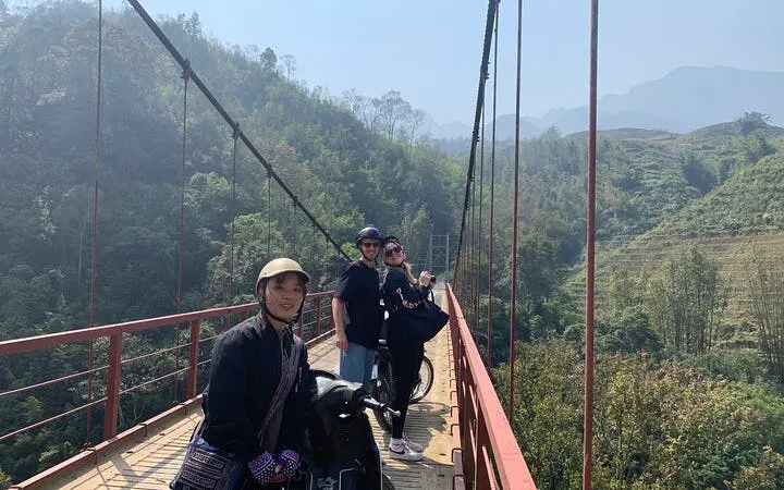 Motorbike riders on a bridge in Sapa, Vietnam, with scenic village and mountain views.