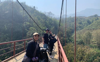 Motorbike riders on a bridge in Sapa, Vietnam, with scenic village and mountain views.