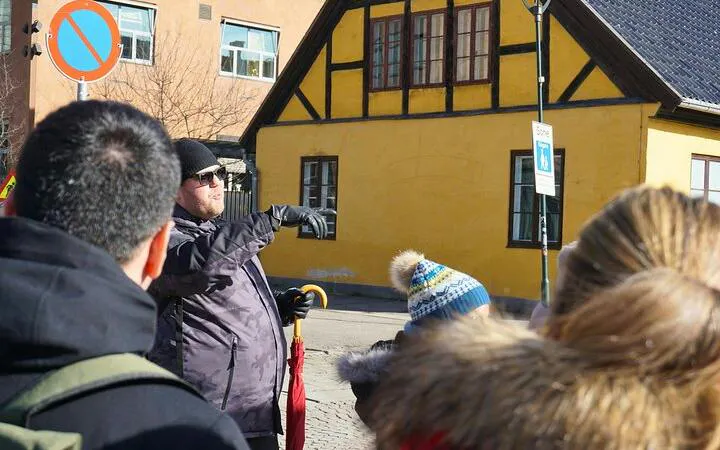 Tour guide leading a group in front of a historic yellow building in Oslo.