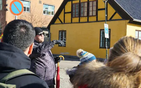Tour guide leading a group in front of a historic yellow building in Oslo.