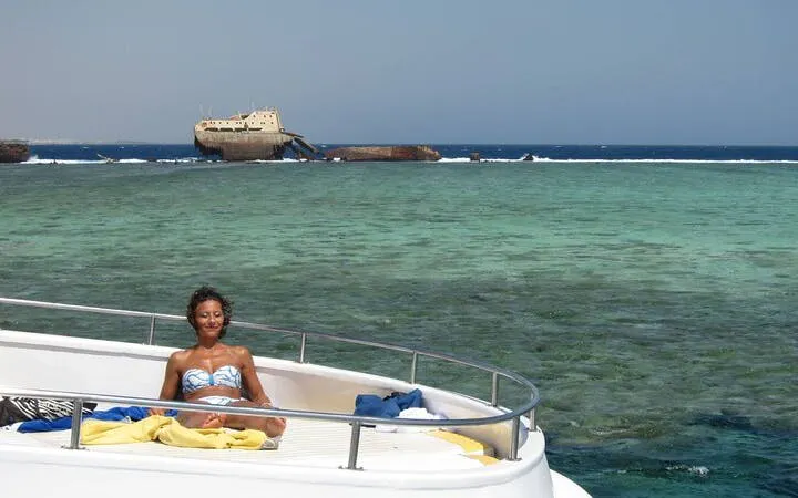 Snorkeler relaxing on boat near Tiran Island, Sharm El Sheikh, with shipwreck in background.