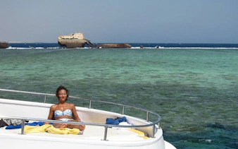 Snorkeler relaxing on boat near Tiran Island, Sharm El Sheikh, with shipwreck in background.