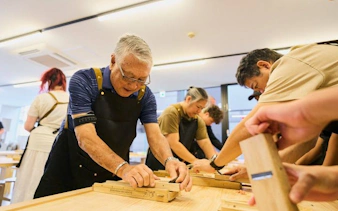 Participants crafting chopsticks at a Tokyo Shinjuku workshop, selecting wood and engraving kanji.