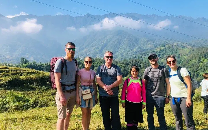 Group of tourists with a local guide in Ta Phin Village, Sapa, with mountains in the background.