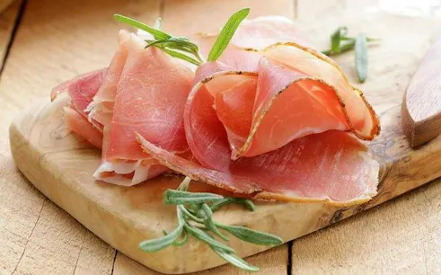 Parma ham slices on a wooden board with rosemary, featured in Parma Food Tour.