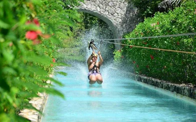 Ziplining over a waterway in Punta Cana with lush greenery and stone bridge.