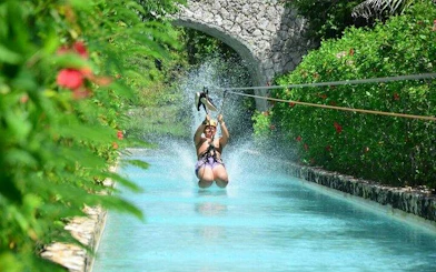 Ziplining over a waterway in Punta Cana with lush greenery and stone bridge.