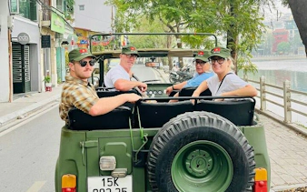 Tourists in an open-top Jeep on a Hanoi city street, part of a guided city tour.