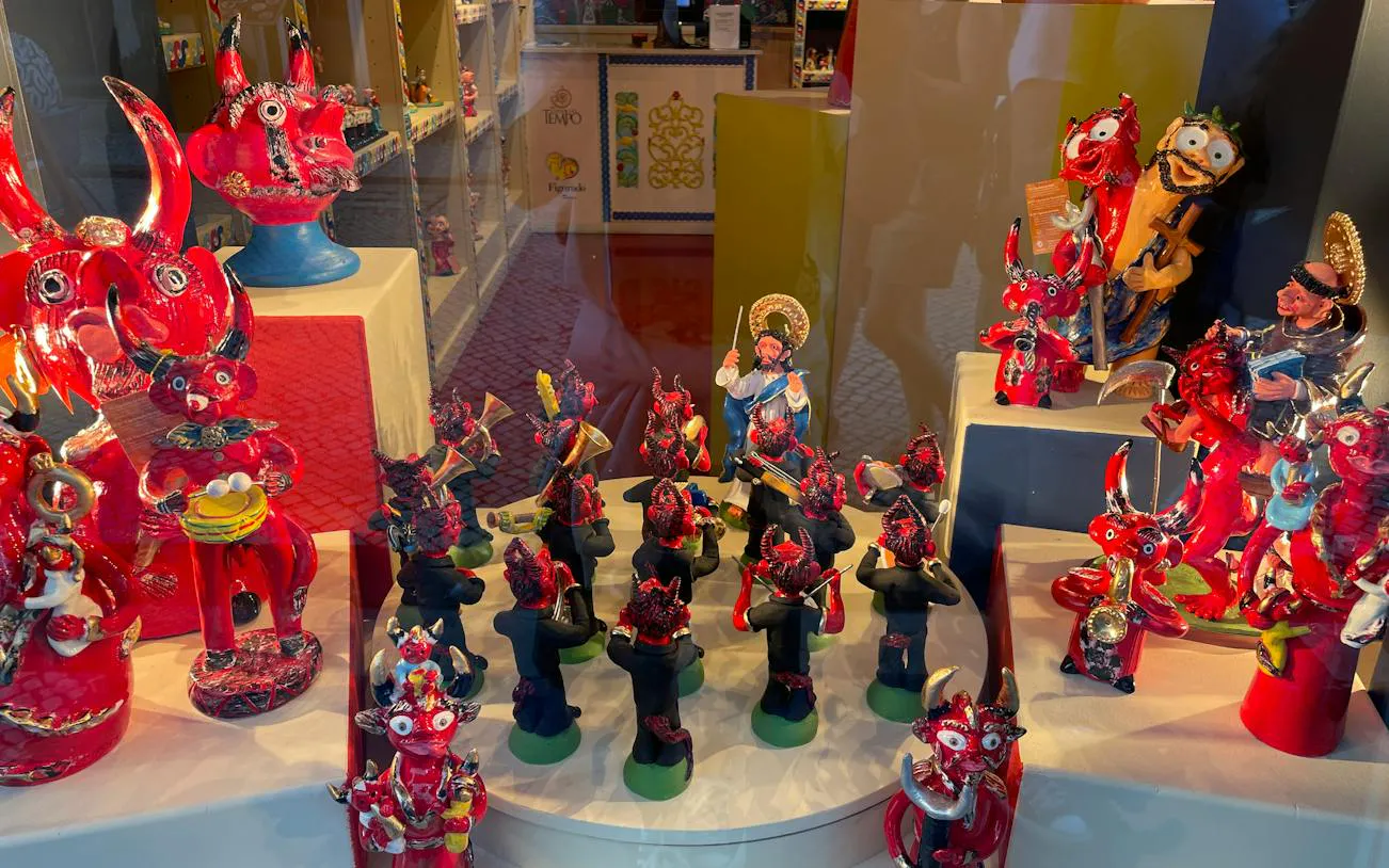 Colorful ceramic figurines in a Lisbon shop window, featuring red devils and musicians, Baixa and Chiado tour.
