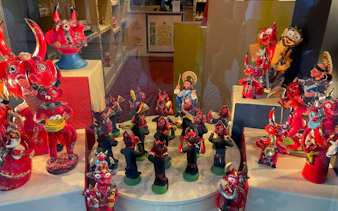 Colorful ceramic figurines in a Lisbon shop window, featuring red devils and musicians, Baixa and Chiado tour.