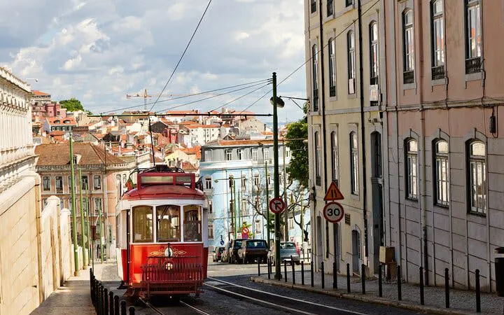 Lisbon tram on a historic street with colorful buildings and cityscape in the background.