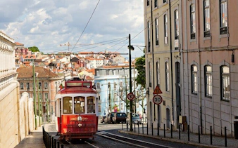 Lisbon tram on a historic street with colorful buildings and cityscape in the background.