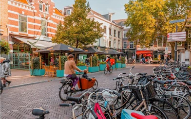 Cyclists ride through a vibrant Utrecht street lined with cafes and parked bicycles.