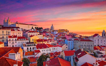Lisbon rooftops at sunset with colorful buildings and distant church domes.